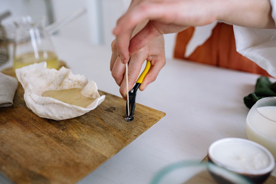 Artesana elaborando velas con pinzas sobre una tabla de madera